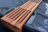 A handcrafted wooden drink holder with multiple slats, resting across a tub, presumably made of cedar wood due to its rich, red color and subtle grain patterns. Sulis Hot Tubs