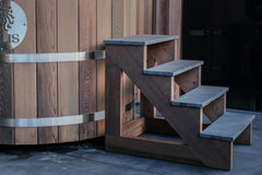 A wooden hot tub named 'Rakaia River Hot Tub' with metal bands and a wooden ladder, set against an outdoor backdrop. Sulis Hot Tubs
