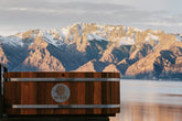 Wooden bathtub with a scenic view of mountains across a body of water, featuring a Sulis logo on the side.