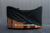 A black canvas hot tub cover fitted over a wooden hot tub, with a corrugated metal wall in the background. Sulis Hot tubs