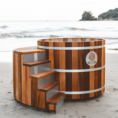 Wooden hot tub with steps on a beach, featuring the Sulis logo.