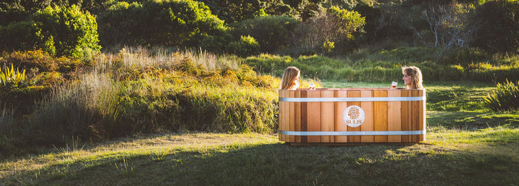 Two people in a wooden Sulis hot tub surrounded by nature