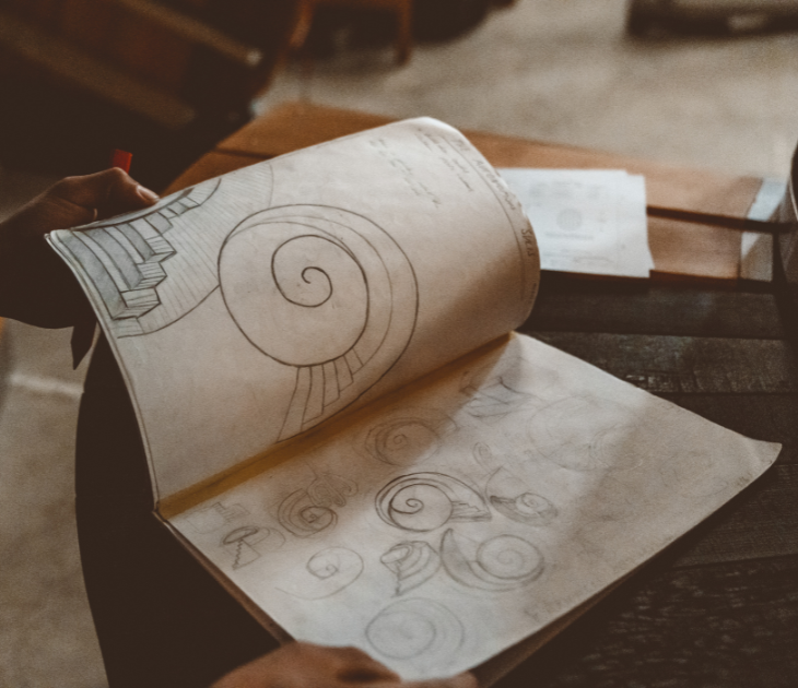 Person holding a rolled-up paper with spiral designs on a wooden table. Sulis hot tubs custom design