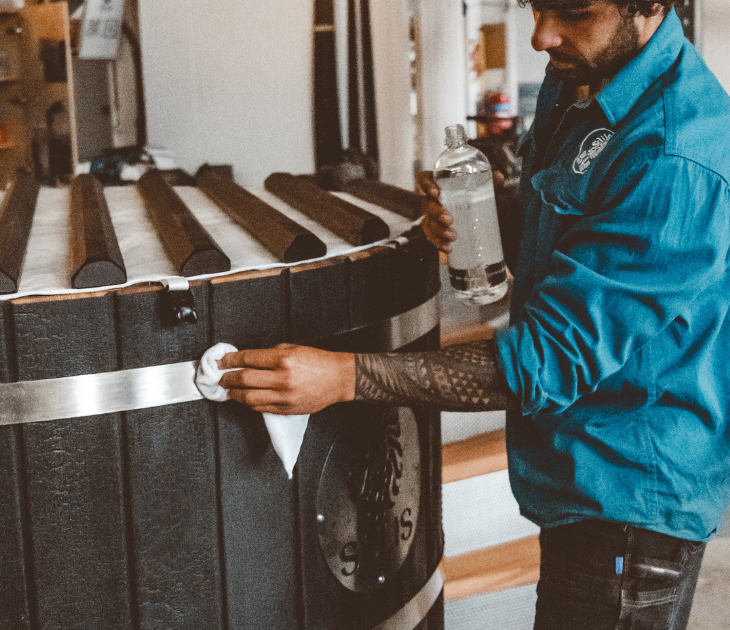 Person in a blue jacket interacting with a large black sulis hot tub in an indoor setting, final touches.