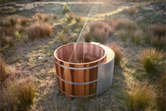 Wooden Sulis hot tub in a natural outdoor setting with grass and sunlight.