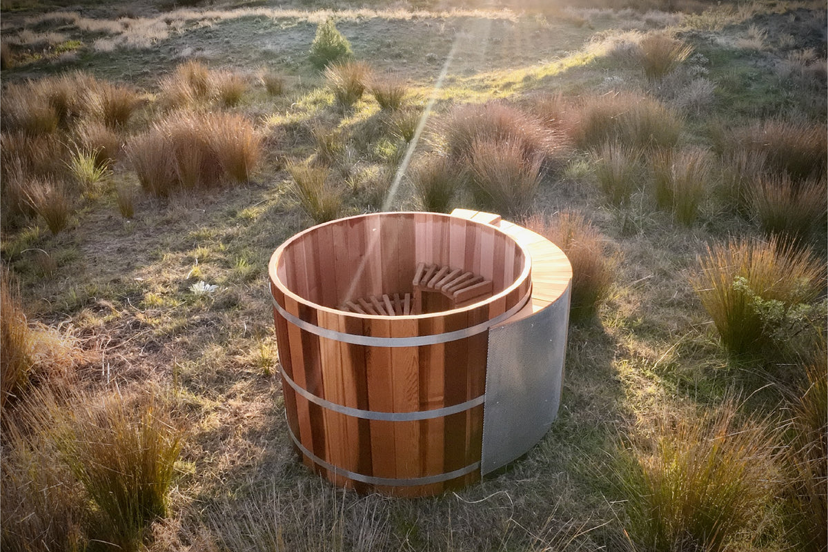 Wooden Sulis hot tub in a natural outdoor setting with grass and sunlight.